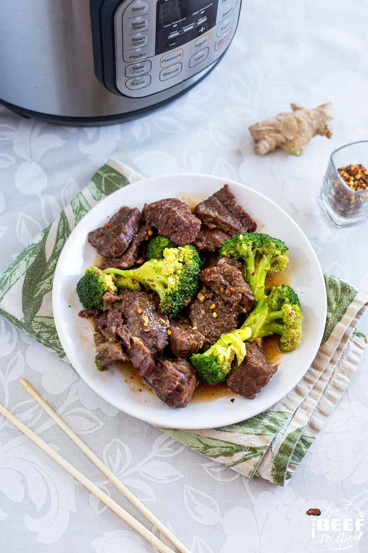 A plate of instant pot beef and broccoli next to chopsticks and the instant pot