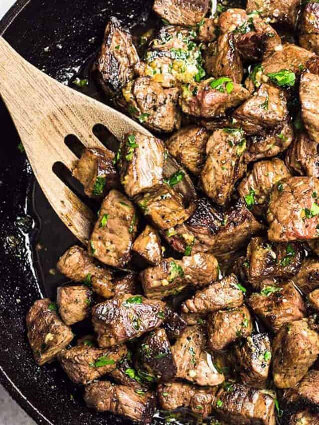 Garlic butter steak bites in a skillet with a wooden slotted spoon