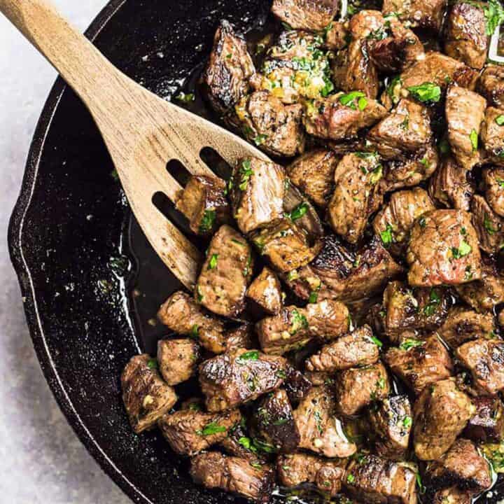 Garlic butter steak bites in a skillet with a wooden slotted spoon