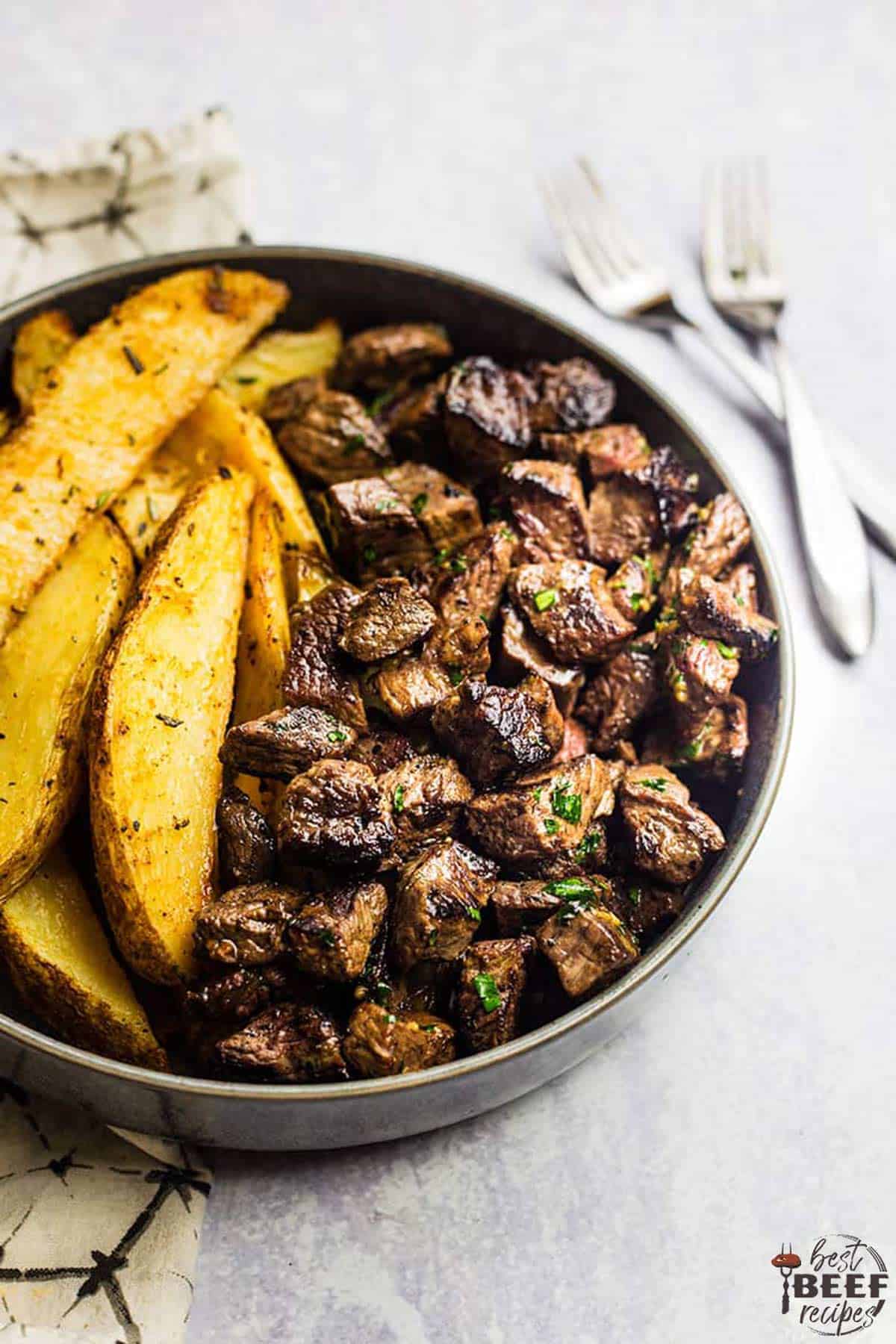 Steak bites in a round dish with baked potato wedges