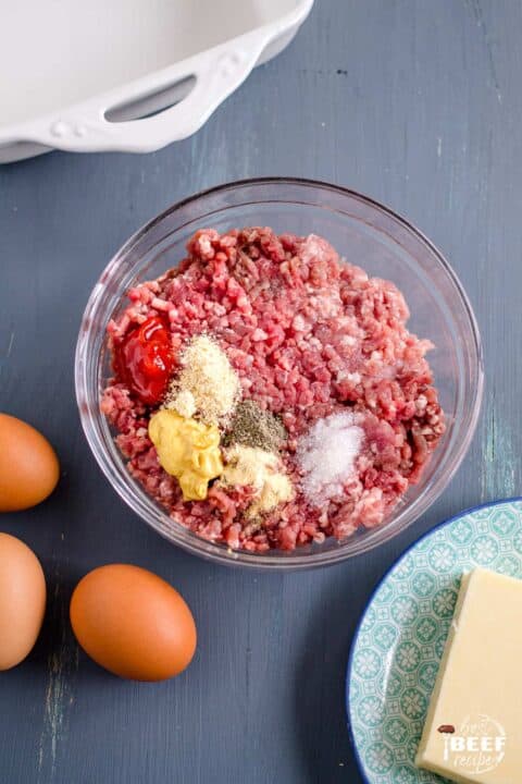 Ground beef and other ingredients in a glass bowl for keto hamburger casserole