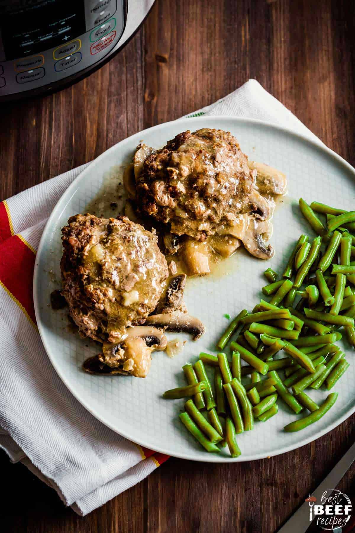 Two salisbury steaks on a white plate with green beans