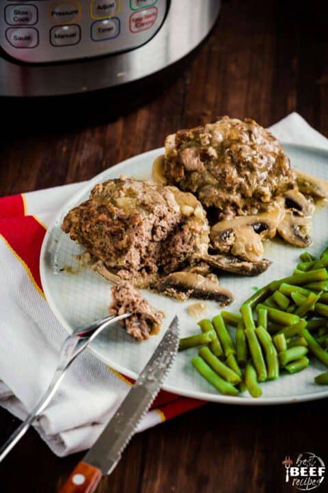 Salisbury steak patties on a plate with green beans and a fork and knife
