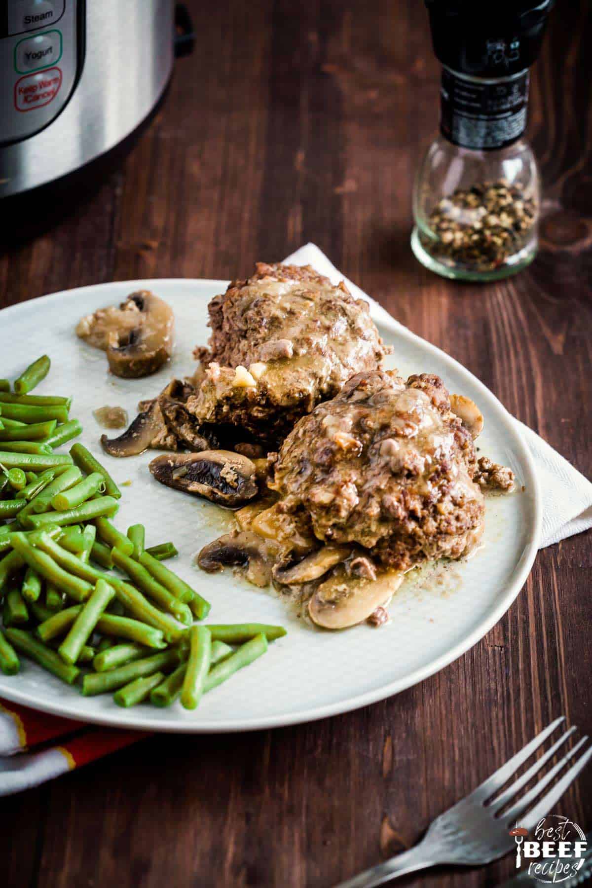 Two salisbury steaks on a white plate with green beans and a fork on the side