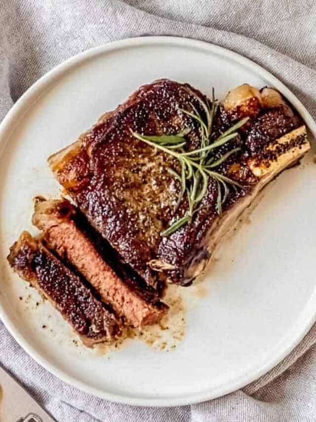 Reverse sear ribeye on a white plate, sliced with sprigs of fresh rosemary on top