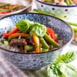 Pepper steak stir fry recipe in a blue and white bowl with fresh basil on top