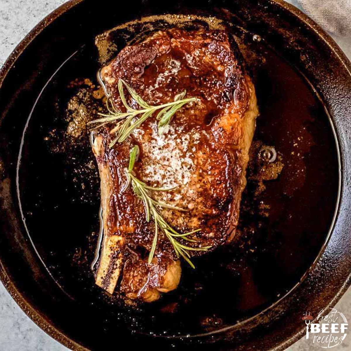 Reverse sear ribeye in a cast iron skillet with rosemary on top