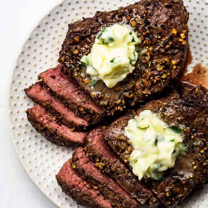 Two air fried steaks on an offwhite plate, cut partially into slices to show the medium rare middle and topped with garlic butter