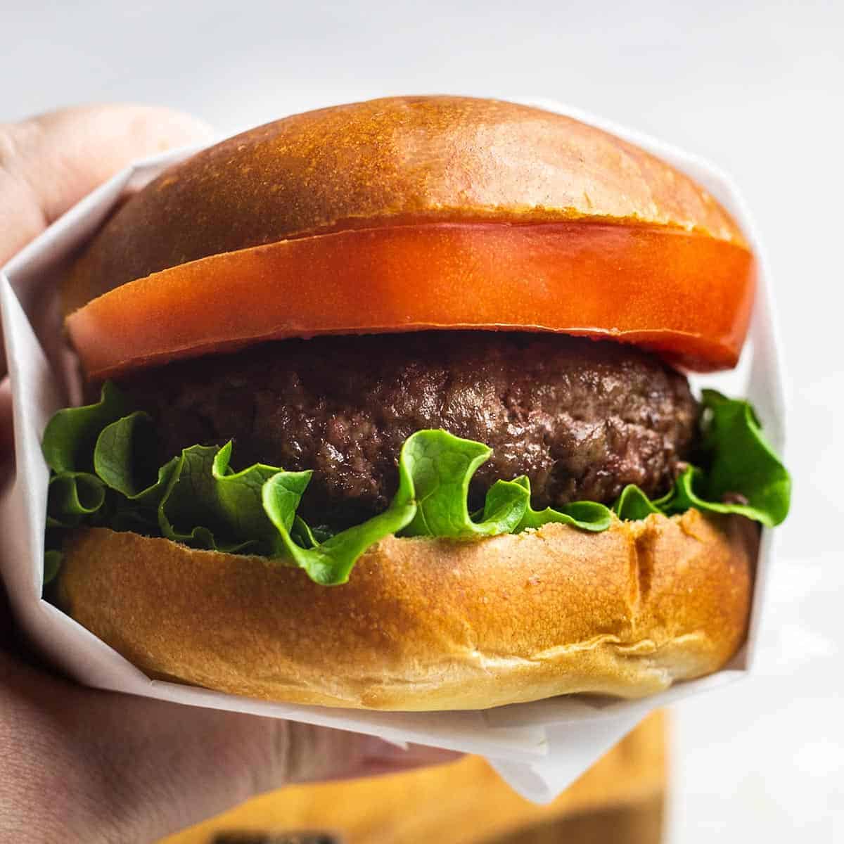 Holding up a garlic butter burger with parchment paper wrapped around it made using air fryer burger recipe