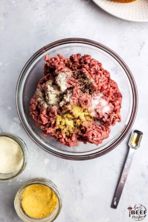 Mixing the ground beef for air fryer burger recipe in a glass bowl with a teaspoon to the side