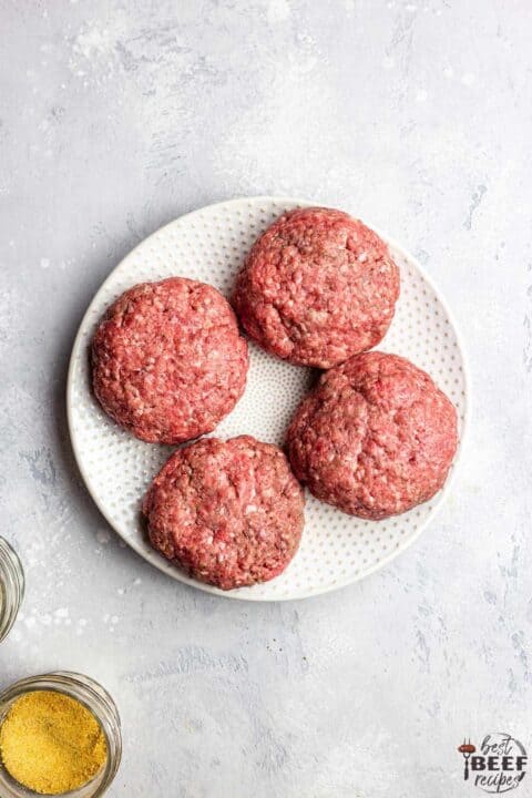 Four uncooked burger patties on a white plate for garlic butter burger