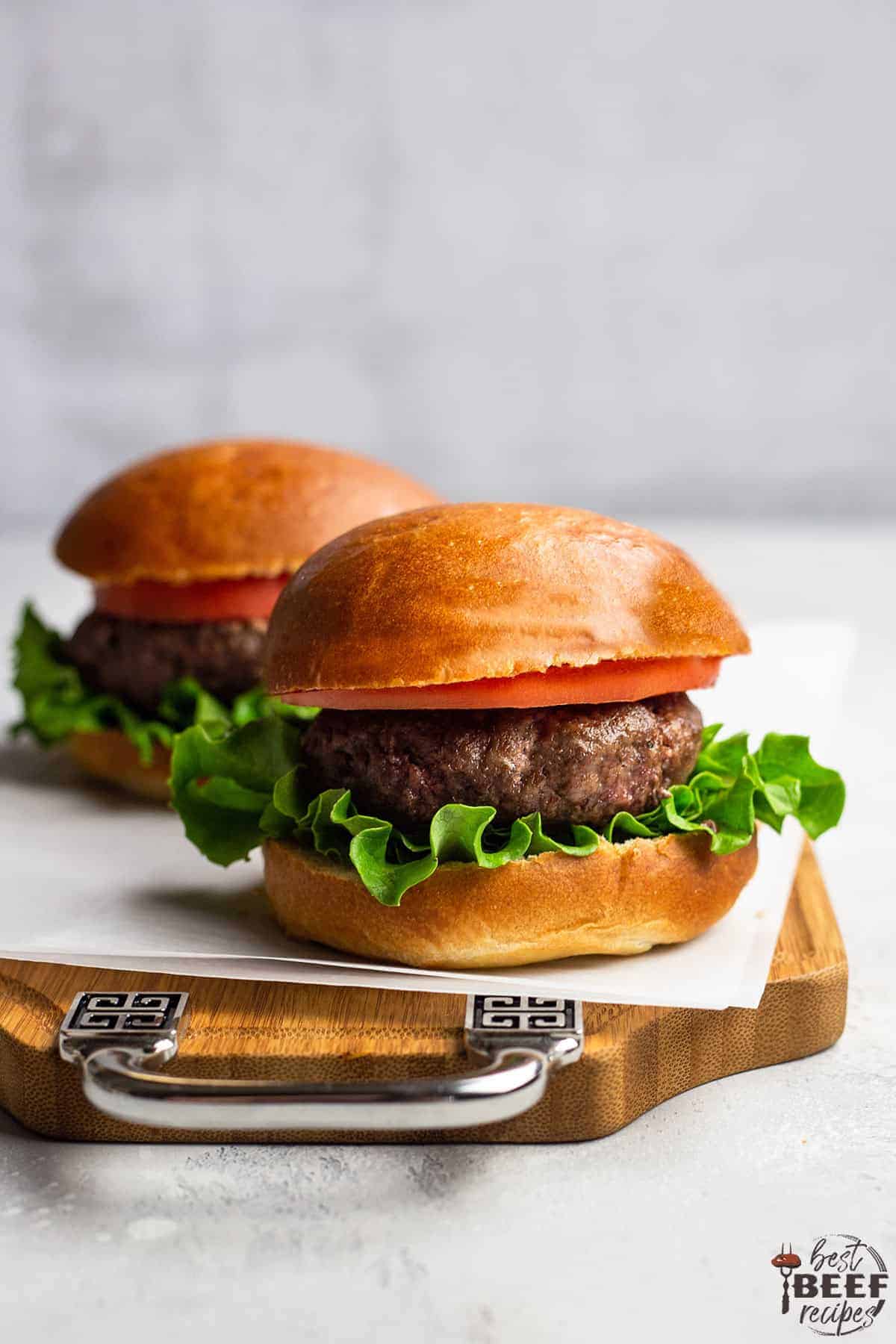 Two air fryer burgers on a wooden serving board