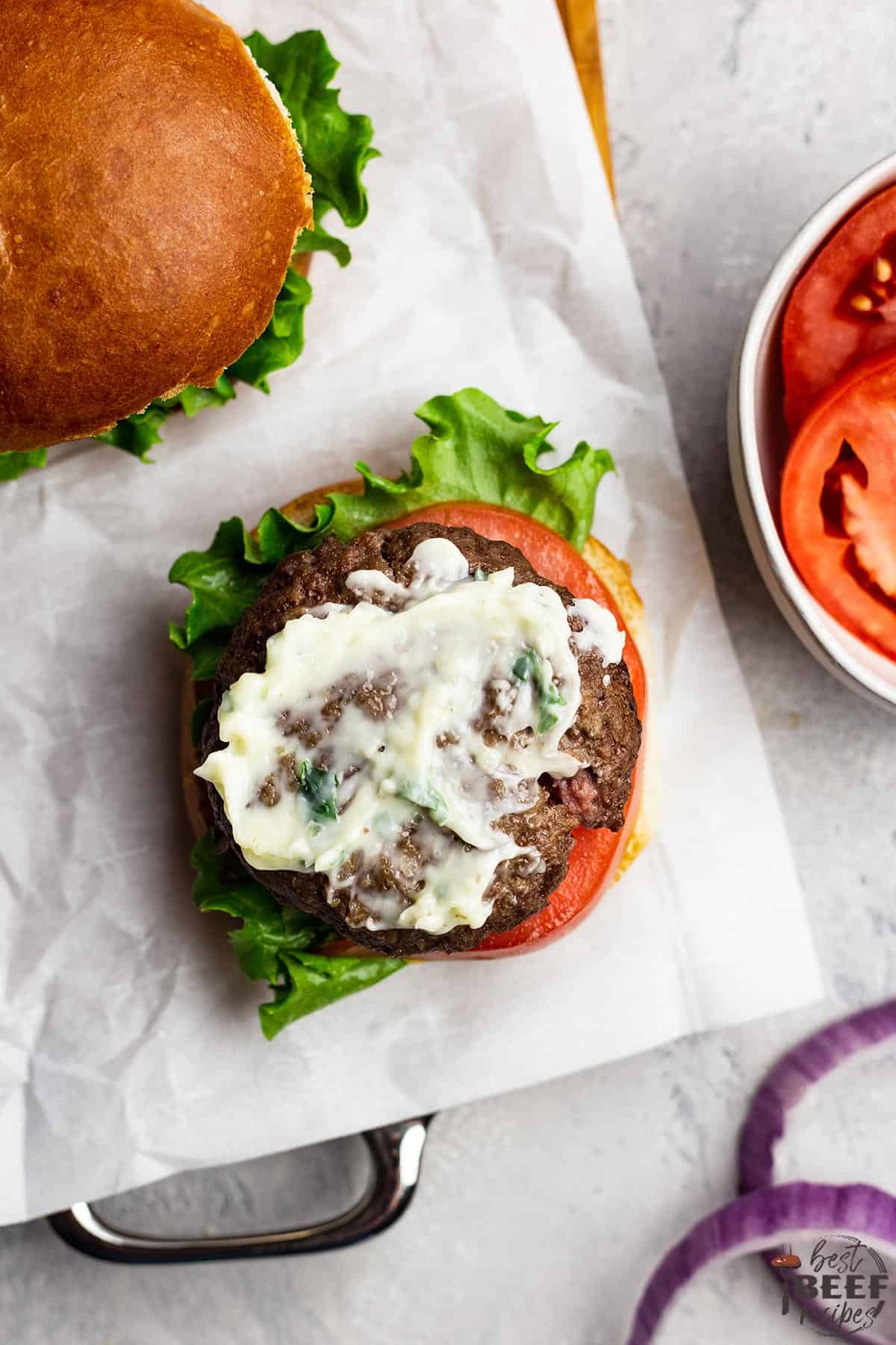 An open-face air fryer burger topped with garlic butter spread and tomatoes to the side in a white bowl