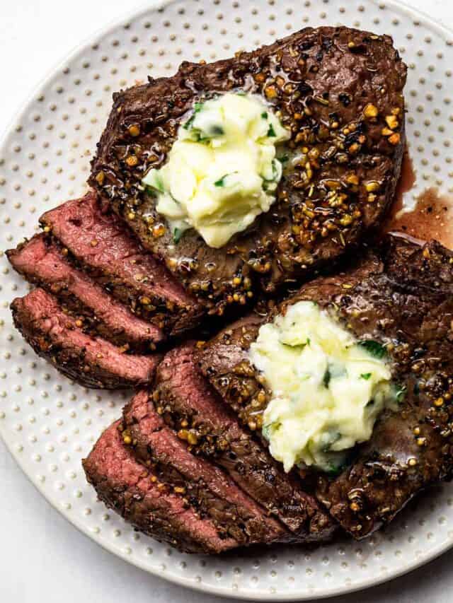 A plate of two air fryer steaks with garlic butter on top, partially cut into slices