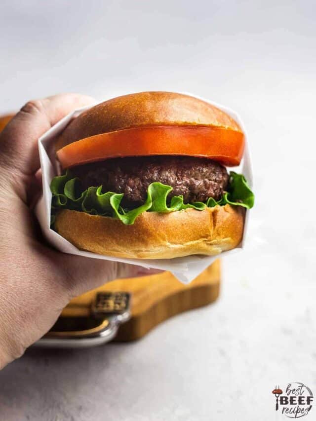 Holding up a garlic butter burger that's wrapped with white paper