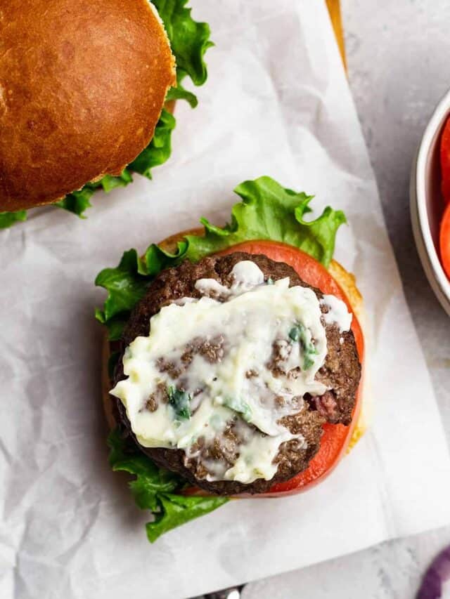 An open-face air fryer burger topped with garlic butter spread and tomatoes to the side in a white bowl