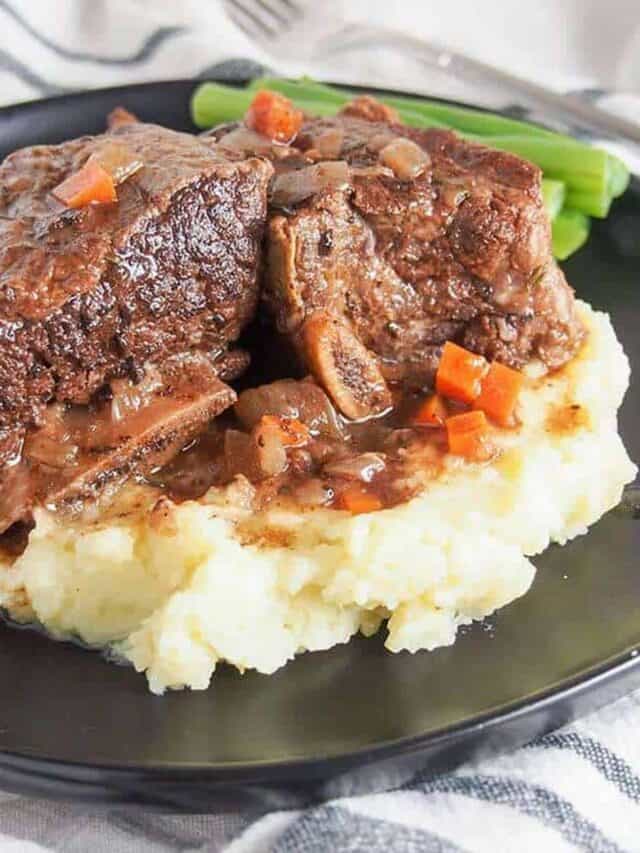 Slow cooker beef short ribs on a black plate over mashed potatoes with green beans on the side