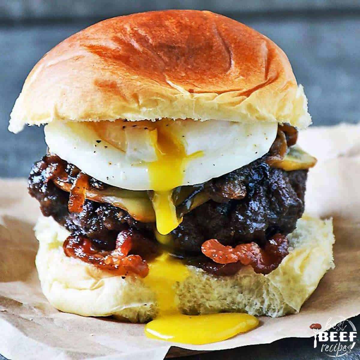 Poached egg burger recipe with a grilled burger, caramelized onions, and egg running down the side on a sheet of butcher paper