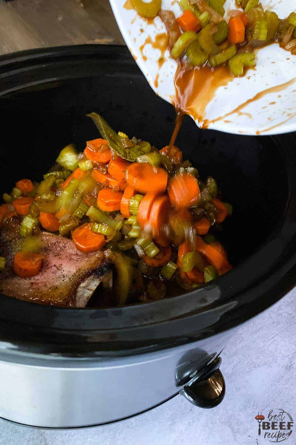 Pouring vegetable mixture over beef ribs in crockpot