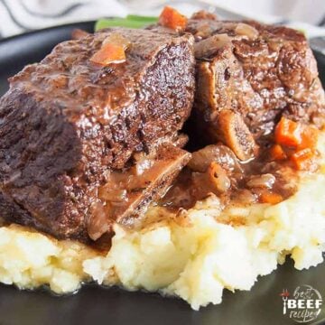 Close up of slow cooker beef ribs on a black plate over a serving of mashed potatoes