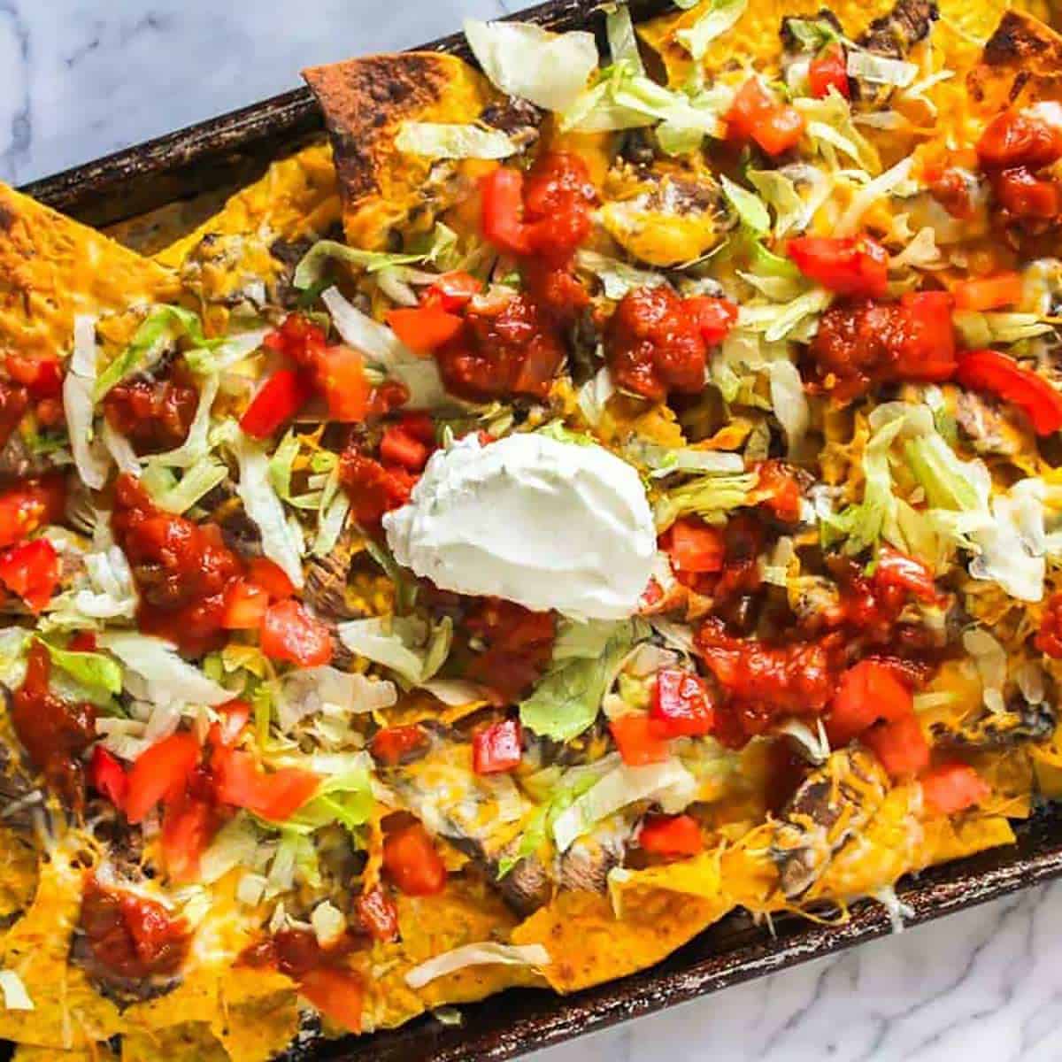 Sheet pan nachos with steak slices, sour cream, tomatoes, and lettuce