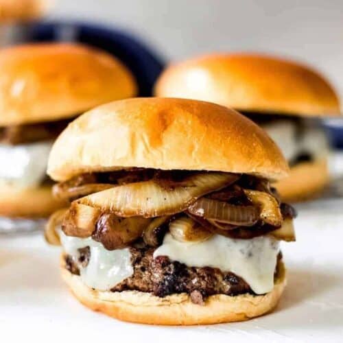 Close up of a mushroom swiss burger on a brioche bun in front of two other burgers