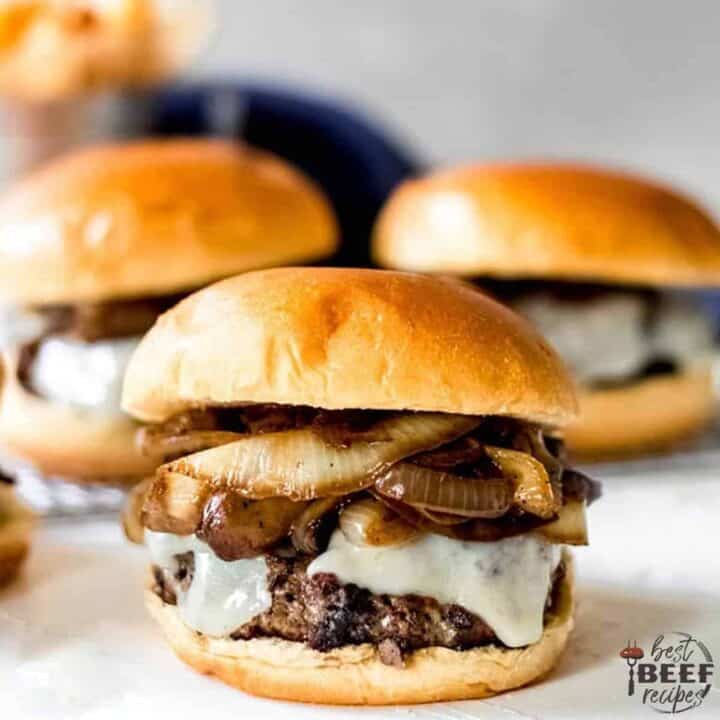 Close up of a mushroom swiss burger in front of two other burgers on brioche buns