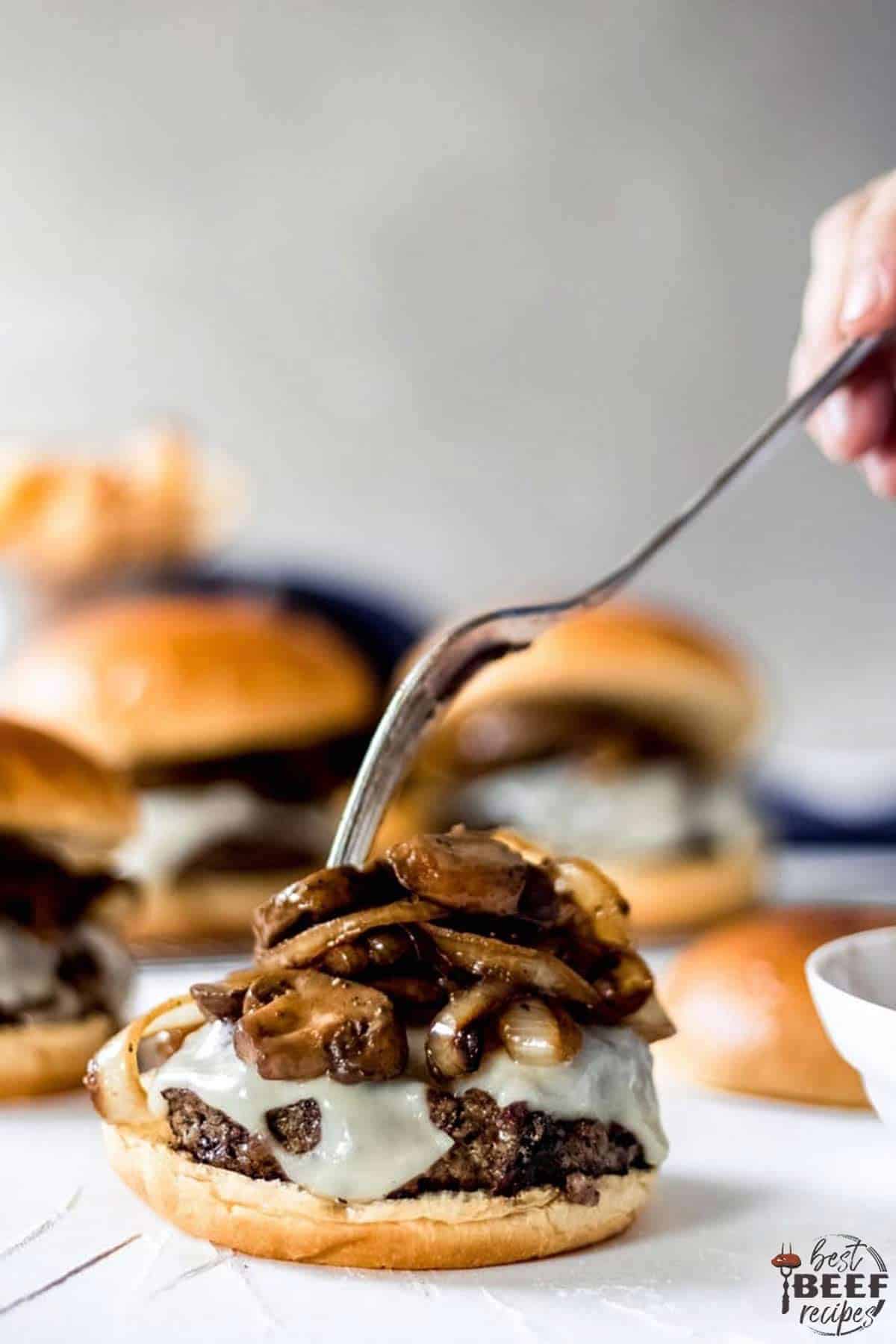 Sticking a fork into the mushrooms and onions on top of a mushroom swiss burger