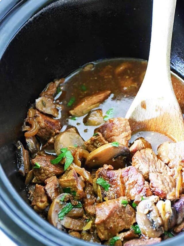 Slow cooker beef tips and gravy in the crockpot after cooking with a wooden spoon