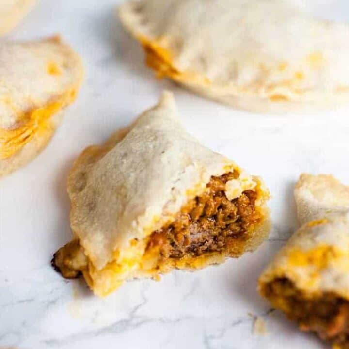 Pastelillos de carne on a white surface, one is split open to show filling