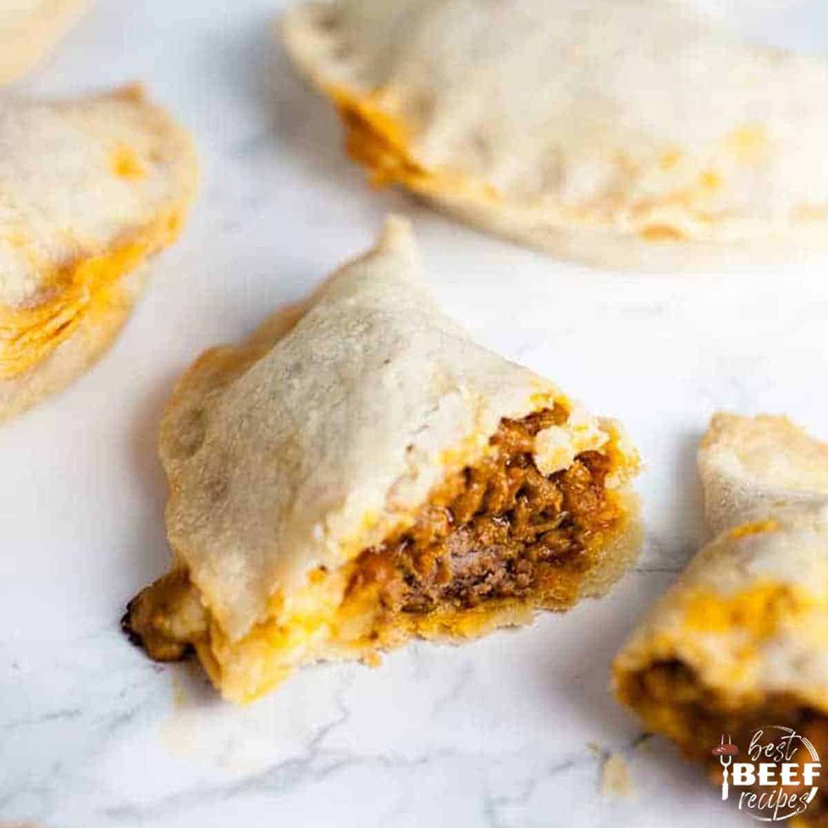 Close up of pastelillos de carne with one split open to show the beef filling