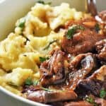 Slow cooker beef tips in a white bowl with mashed potatoes