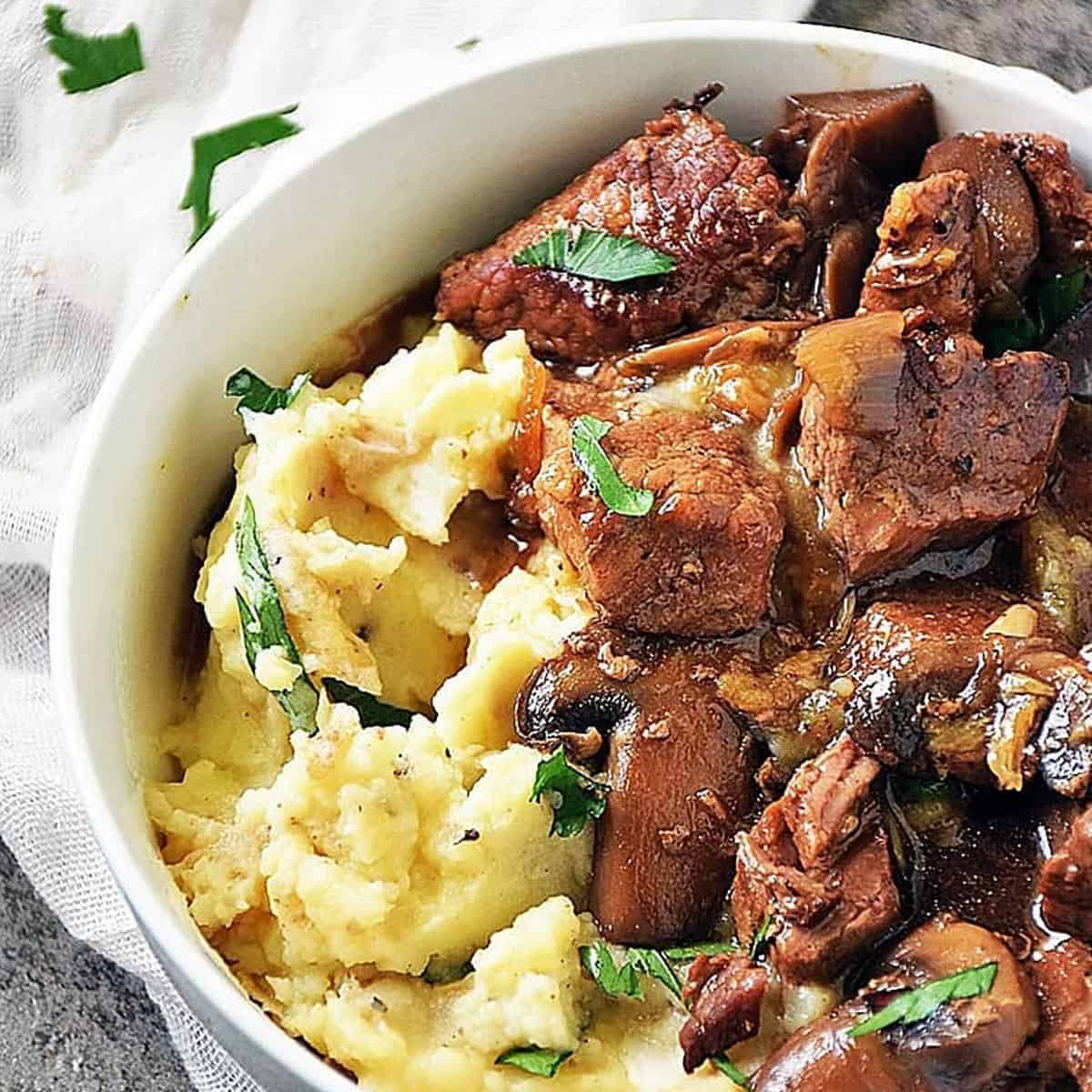 A white bowl of beef tips and gravy over mashed potatoes