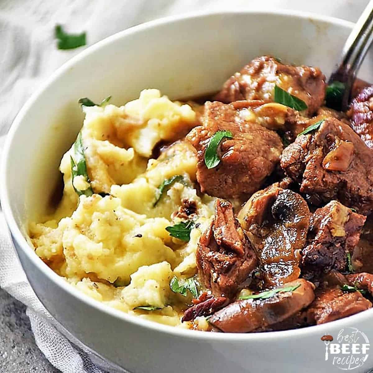 Beef tips and gravy over mashed potatoes in a white bowl