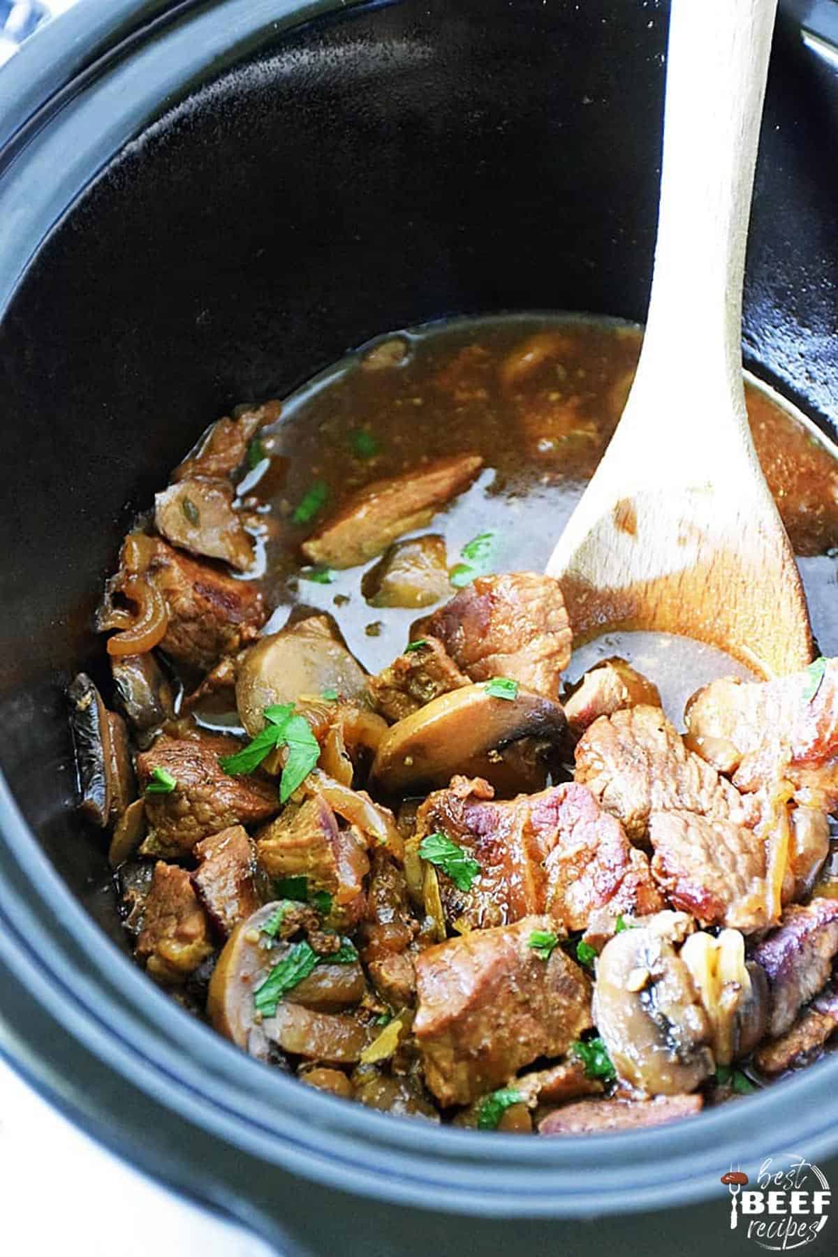 Slow cooker beef tips and gravy in the crockpot after cooking with a wooden spoon