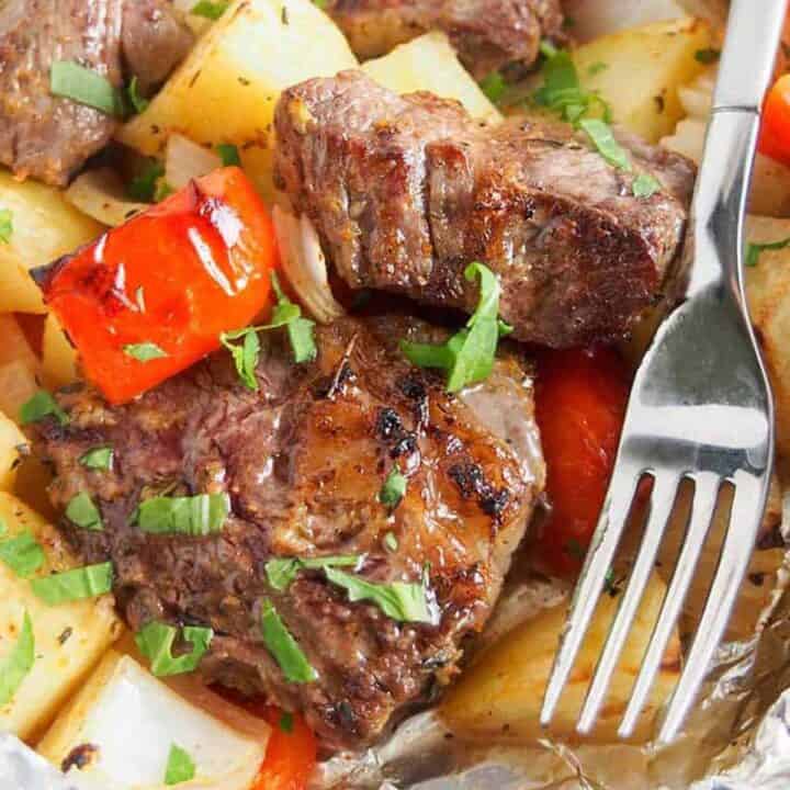 Close up of cooked steak, peppers, and potatoes next to a fork