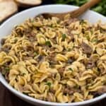 Close up of instant pot beef stroganoff in a white dish with a wooden spoon