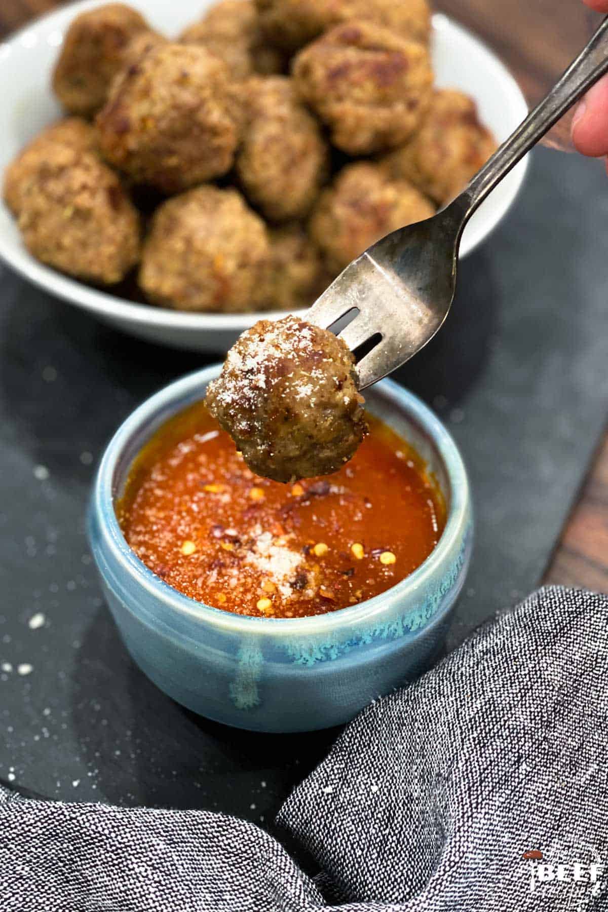 Dipping a meatball in dipping sauce with parmesan on top