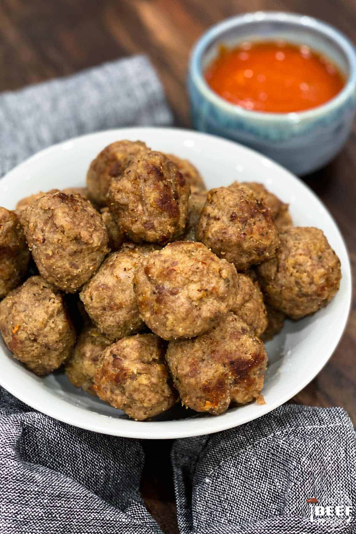 Instant pot meatballs stacked on a white dish with a side of dipping sauce