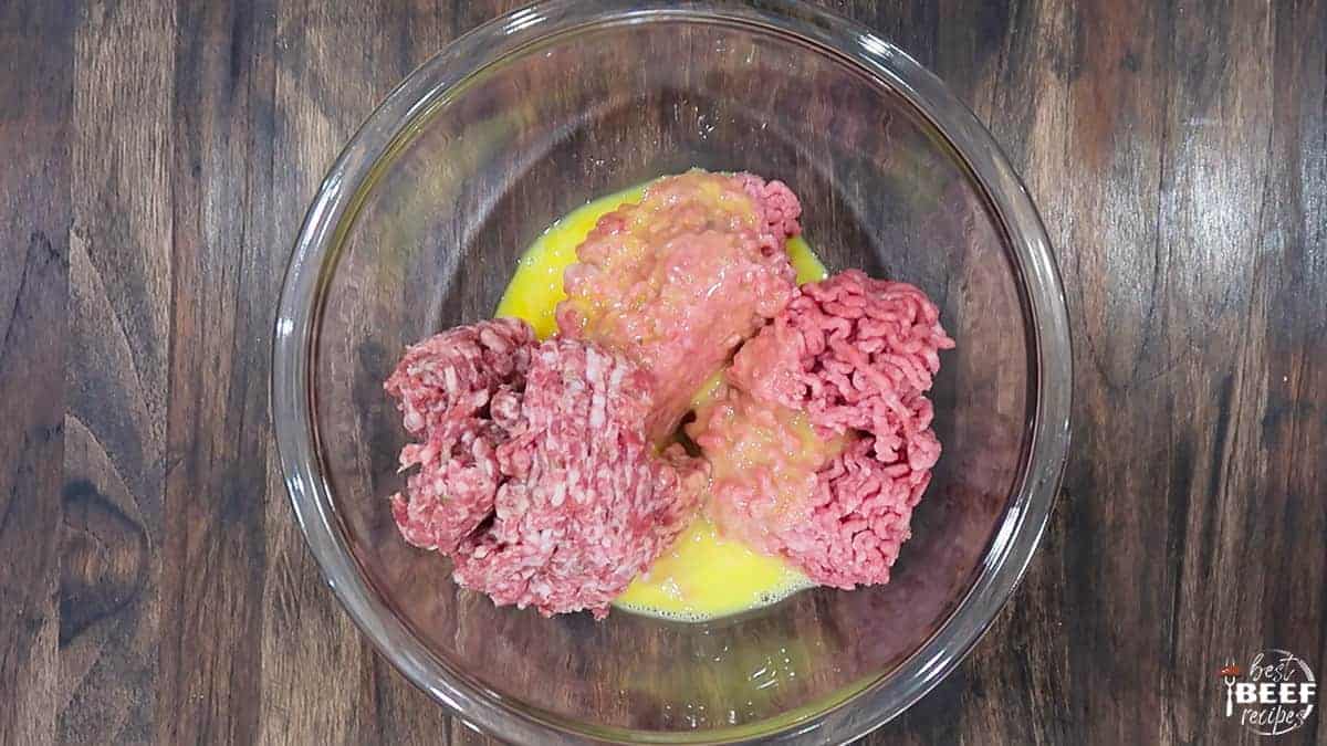 Mixing egg into ground beef in a glass bowl