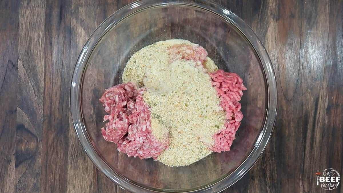 Seasonings and breadcrumbs over ground beef in a glass bowl