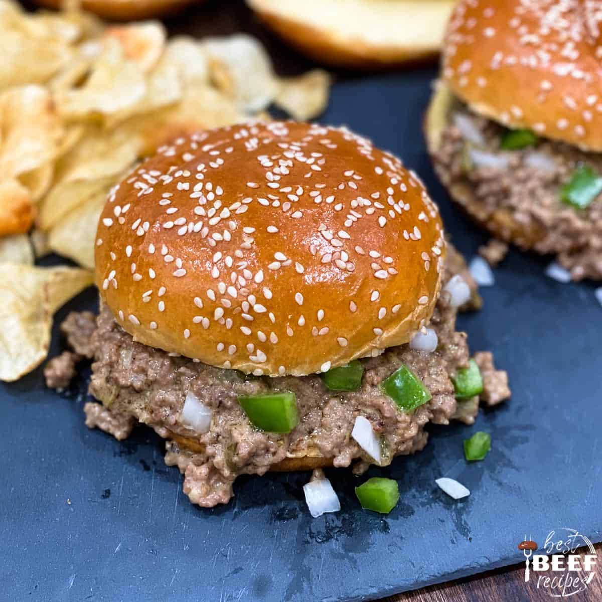 Close up of a Philly cheesesteak sloppy joe next to chips on a black surface