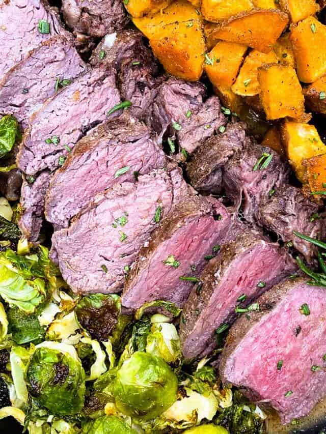 Close up of sous vide tenderloin sliced next to brussels sprouts and sweet potatoes in a skillet