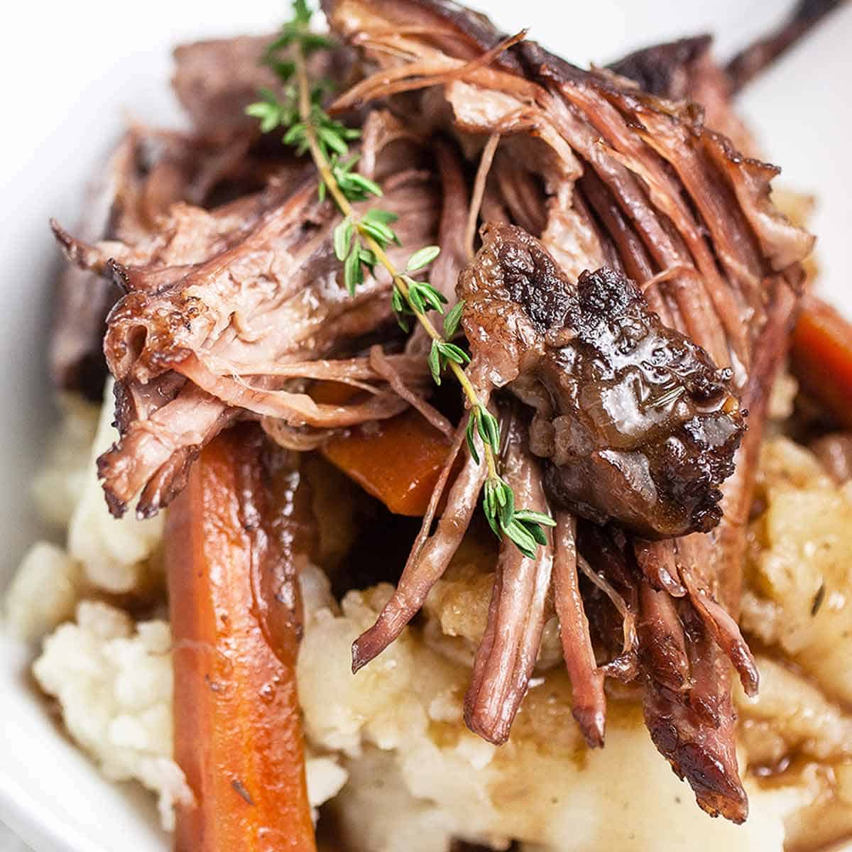 Close up of Dutch Oven Pot Roast with a sprig of rosemary on top and mashed potatoes underneath