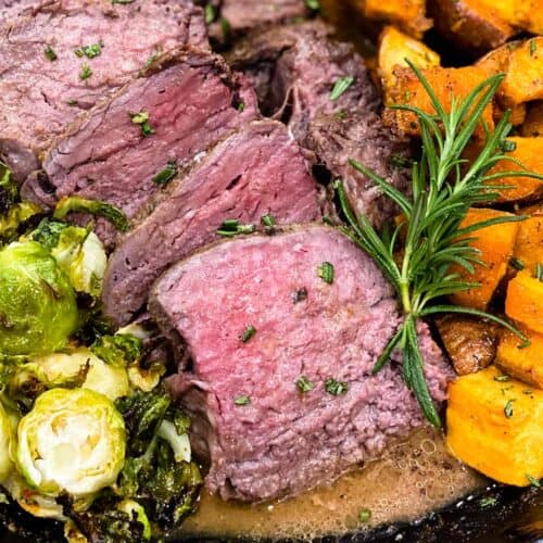 Sous vide tenderloin sliced in a skillet with sweet potatoes, garlic butter, and brussels sprouts