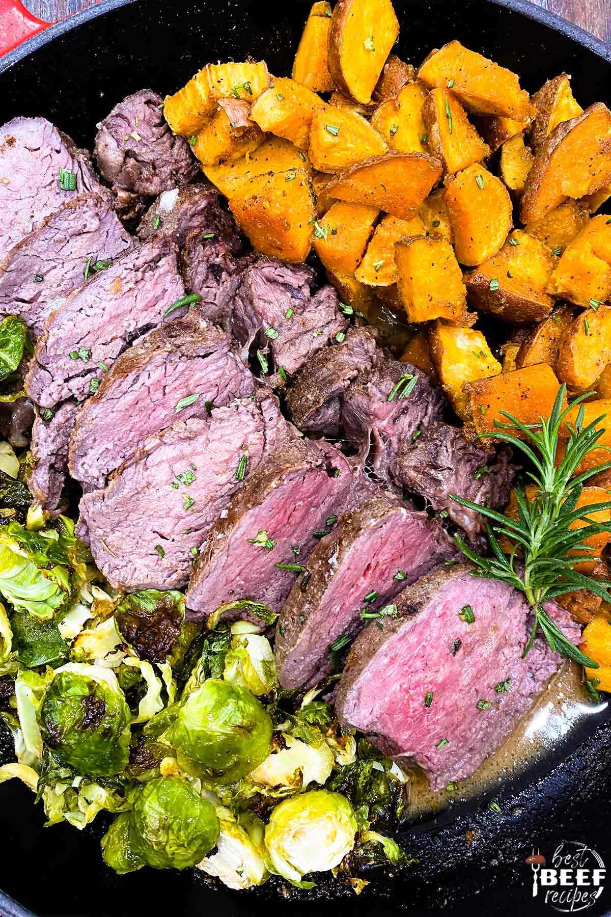 Close up of sous vide tenderloin sliced next to brussels sprouts and sweet potatoes in a skillet