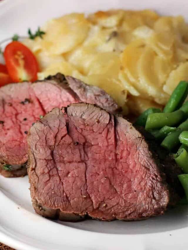 Two slices of tenderloin next to tomatoes, potatoes, and green beans on a plate