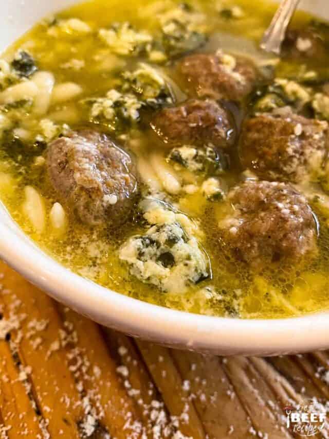Italian wedding soup in a white bowl up close with a spoon