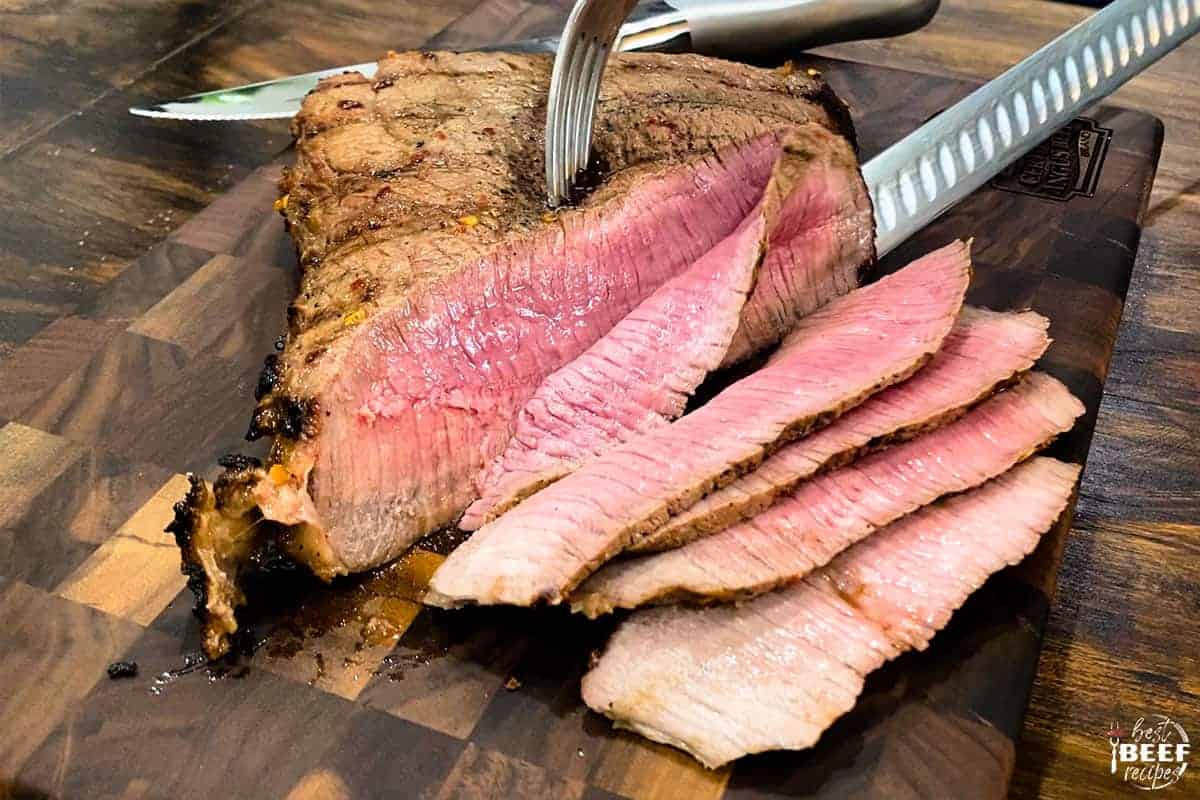 Slicing london broil with a fork and knife on a cutting board