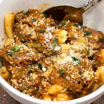 Close up of Instant Pot steak pizzaiola in a white bowl with a spoon over pasta